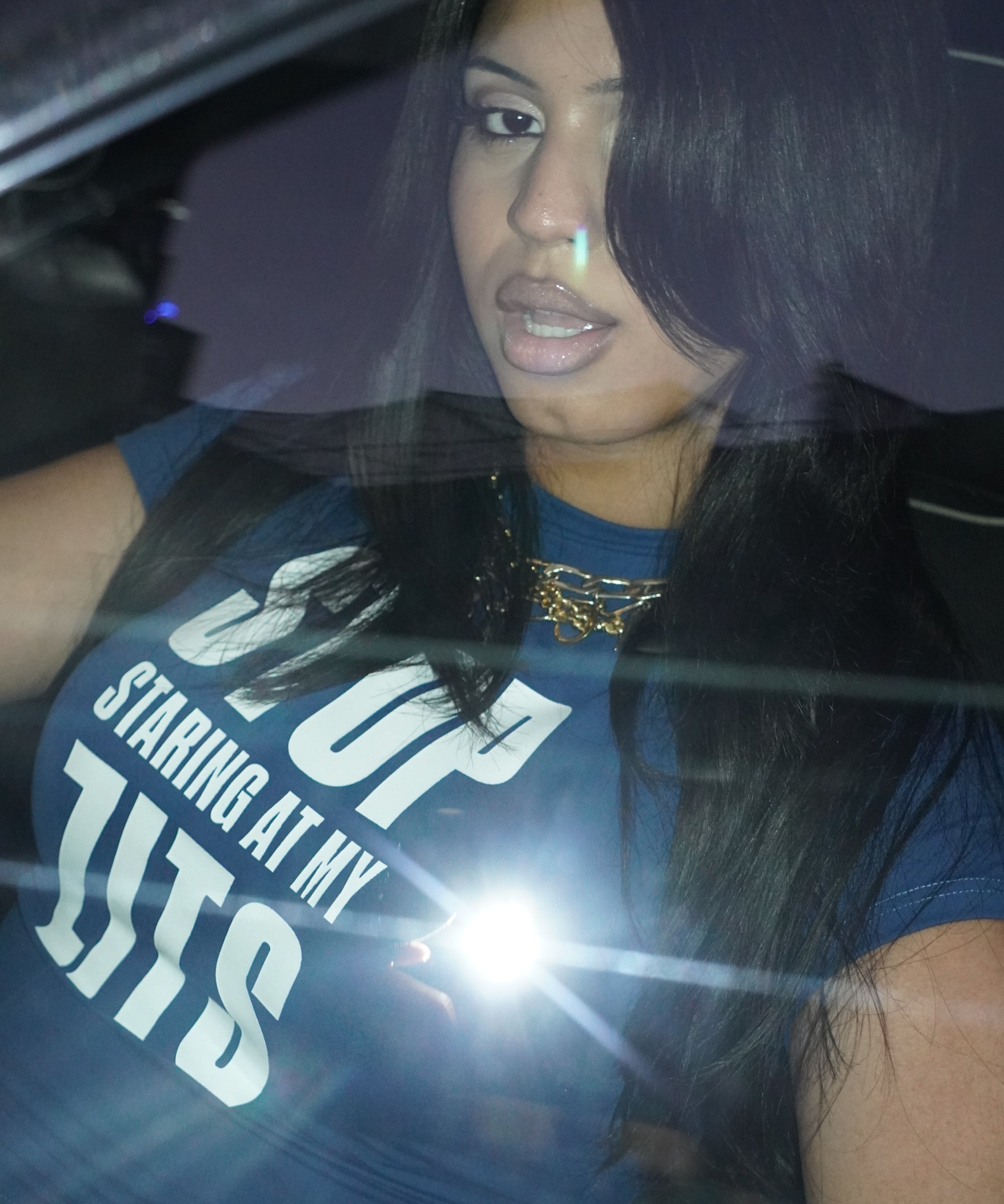 Flash photo of a person seated in a car at night wearing the Topicals Stop Staring At My Zits tee.