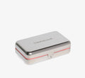 Skincare travel case from Topicals shown as a closed silver metal tin with embossed branding and a pink trim detail on a white background.